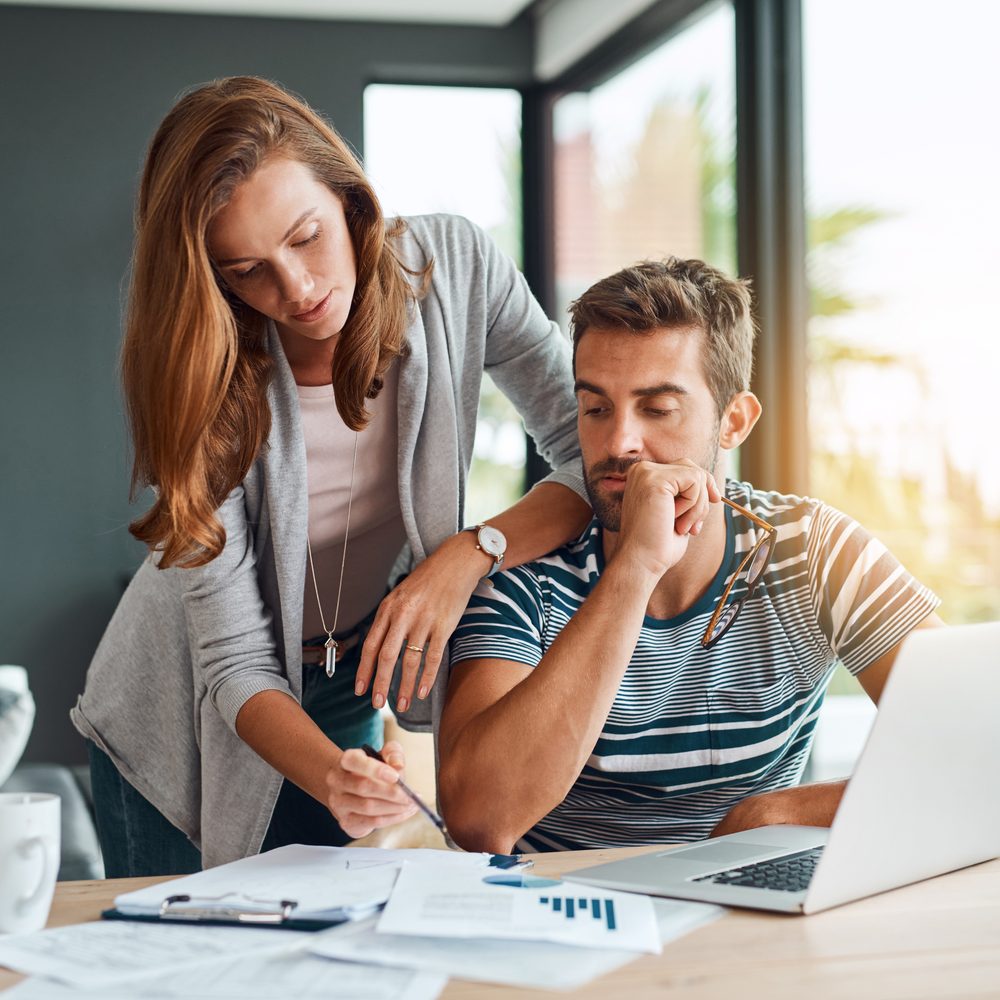 Propriétaire de 35 ans comparant des solutions d’épargne sur un ordinateur portable, entouré de documents financiers.