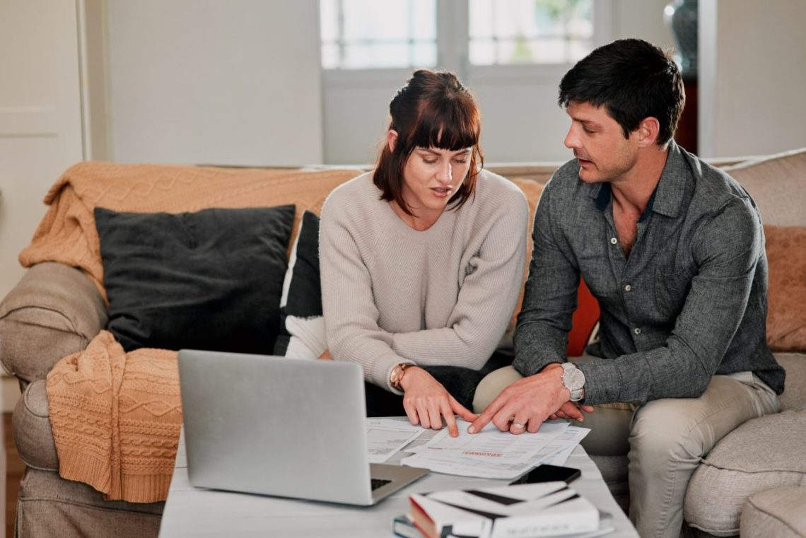 Jeune couple examinant des documents de crédit immobilier avec une calculatrice à la table de la cuisine.