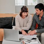 Jeune couple examinant des documents de crédit immobilier avec une calculatrice à la table de la cuisine.