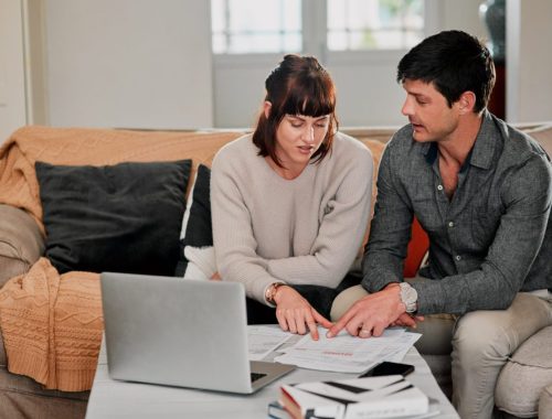 Jeune couple examinant des documents de crédit immobilier avec une calculatrice à la table de la cuisine.