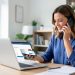 Une femme échange au téléphone tout en consultant un paiement en attente sur un ordinateur portable dans un bureau lumineux.