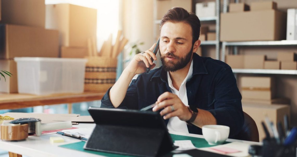 Entrepreneur en dropshipping examinant les bénéfices de sa boutique en ligne sur un ordinateur et un carnet de notes.